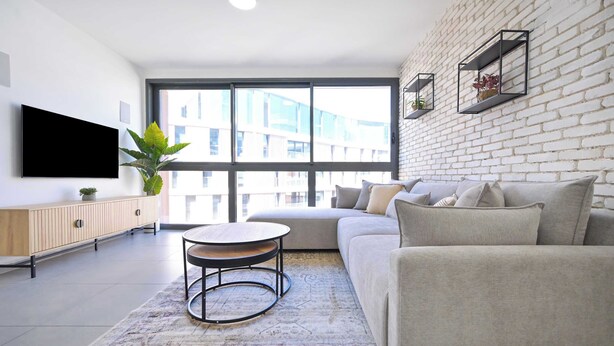 Un salon moderne avec une grande fenêtre, un téléviseur à écran plat, un canapé, une table basse et une plante.