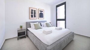 Une chambre à coucher moderne avec un grand lit, une table de chevet agrémentée d’une plante et deux œuvres d’art encadrées accrochées au mur.