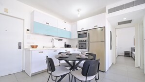 Une cuisine moderne avec des meubles blancs et bleus, un réfrigérateur en acier inoxydable et un coin repas comprenant quatre chaises et une table ronde.