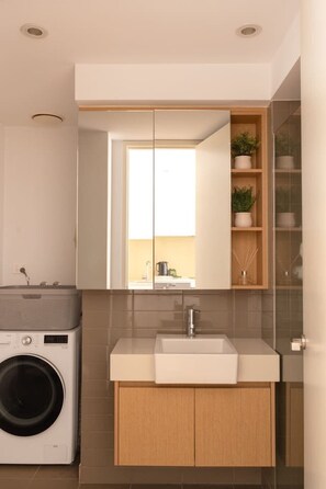 A modern bathroom with a built-in washing machine, a sink, and a mirror. - Coastal Retreat Steps to Beach (Port Melbourne)