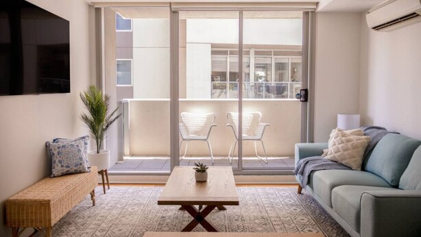 A modern living room with a sofa, a coffee table, and a balcony with two chairs. - Coastal Retreat Steps to Beach (Port Melbourne)