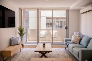 A modern living room with a sofa, a coffee table, and a balcony with two chairs. - Coastal Retreat Steps to Beach (Port Melbourne)
