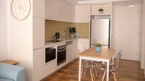 A compact kitchen with a dining area, including a table and chairs, a coffee machine, and a refrigerator. - Coastal Retreat Steps to Beach (Port Melbourne)