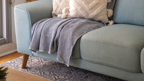 A light blue sofa with a patterned throw blanket and decorative pillows, a small side table with a lamp, and a patterned rug on a wooden floor. - Coastal Retreat Steps to Beach (Port Melbourne)