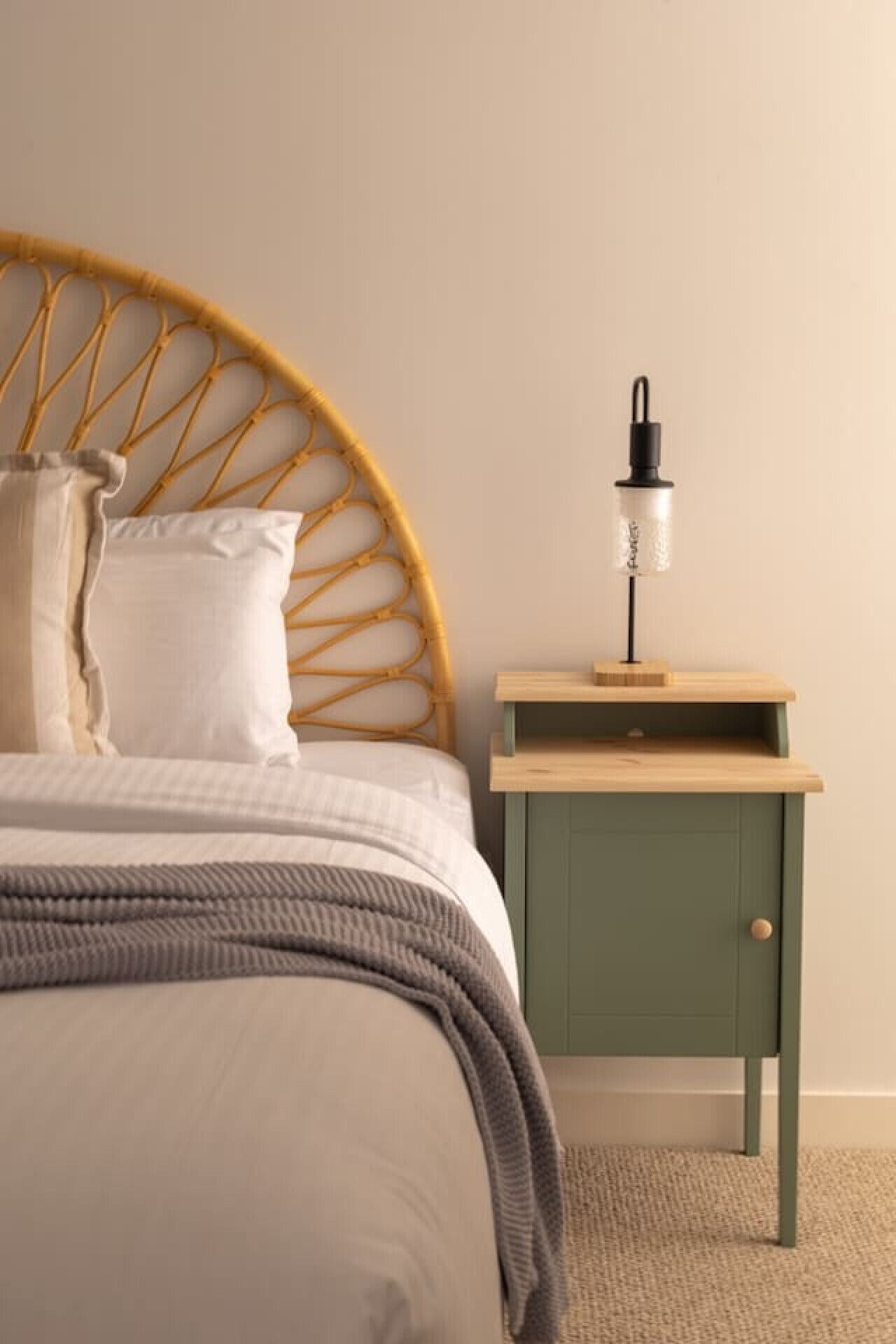 A bed with a woven headboard, a bedside table with a lamp, and a green cabinet.