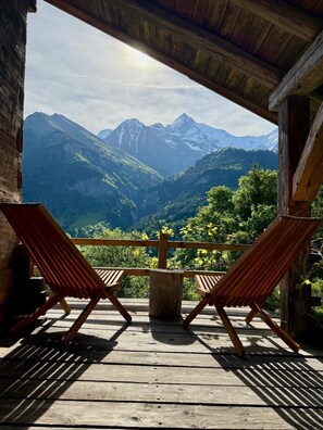 A wooden deck with two lounge chairs facing a mountainous landscape.