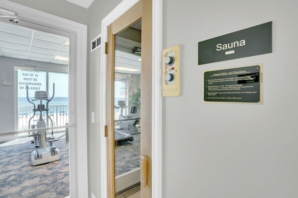 A room with a sauna sign, a control panel, and a view of a balcony with exercise equipment.