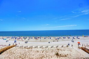 A beach with a wooden boardwalk, sandy dunes, and a clear blue sky.