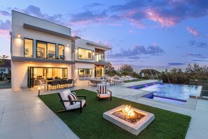 Una casa moderna de dos pisos con piscina, mobiliario exterior y una chimenea.