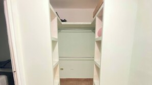 Un pasillo estrecho con suelo de baldosas y paredes blancas, que conduce a una habitación con una puerta al final.