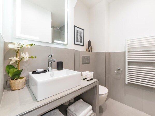 A modern bathroom with a white sink, mirror, and toilet. There is a towel rack and a small plant on the counter.