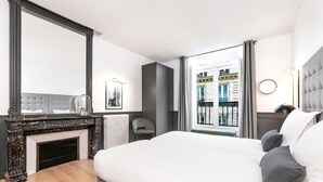 Quarto de hotel moderno com uma cama grande, lareira, vista para edifícios e janela com cortinas.