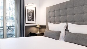 Ein Hotelzimmer mit einem großen Bett, einem Nachttisch mit Lampe, einem gerahmten Bild an der Wand und Blick auf die Stadt durch das Fenster.