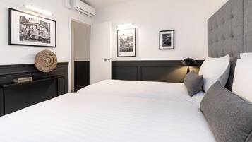 Een moderne hotelkamer met een groot bed, een donker hoofdeinde en twee nachtkastjes. Er hangen ingelijste foto’s aan de muur en boven het bed bevindt zich een airconditioner.