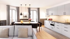 Eine moderne Küche mit grauen Schränken, eine Essecke mit Tisch und Stühlen sowie ein graues Sofa mit gemusterten Kissen.