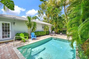 Une piscine entourée de chaises longues, de palmiers et d’une maison avec un toit en tuiles.