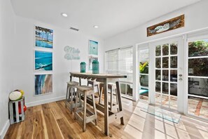 Une cuisine avec un plancher en bois, une table à manger avec des tabourets, et une vue sur un espace extérieur accessible par une porte vitrée.