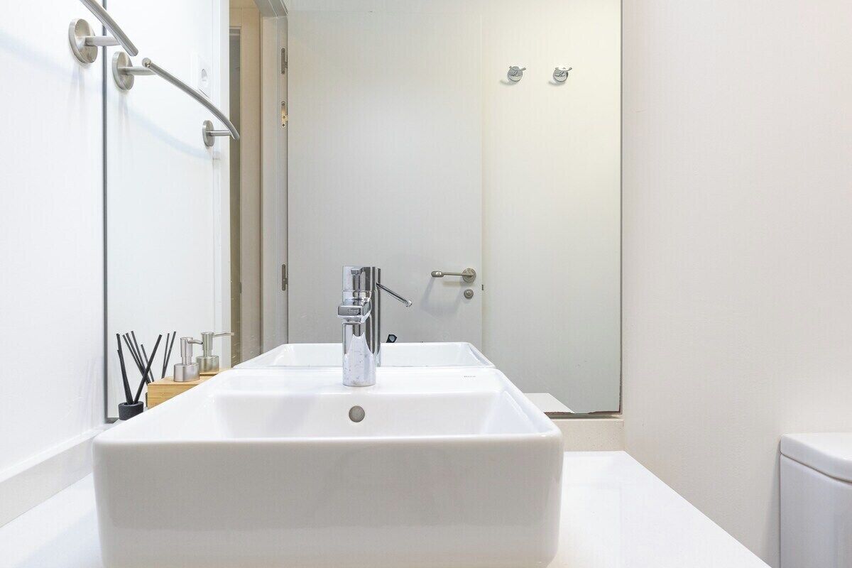 A modern bathroom with a large white sink, a mirror, and a shower area.