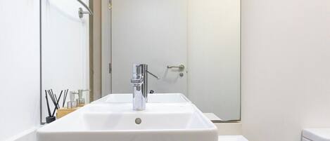 A modern bathroom with a large white sink, a mirror, and a shower area.
