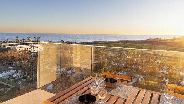 Een balkon met een tafel gedekt voor twee, met uitzicht op een kustlandschap onder een heldere lucht.