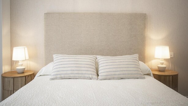 Una cama bien tendida con dos almohadas y dos lámparas de noche en mesitas a juego.
