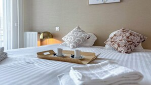 Ein ordentlich bezogenes Bett mit einer Tablett voller Handtücher und einer Tasse, einer Lampe und einem Bild an der Wand.