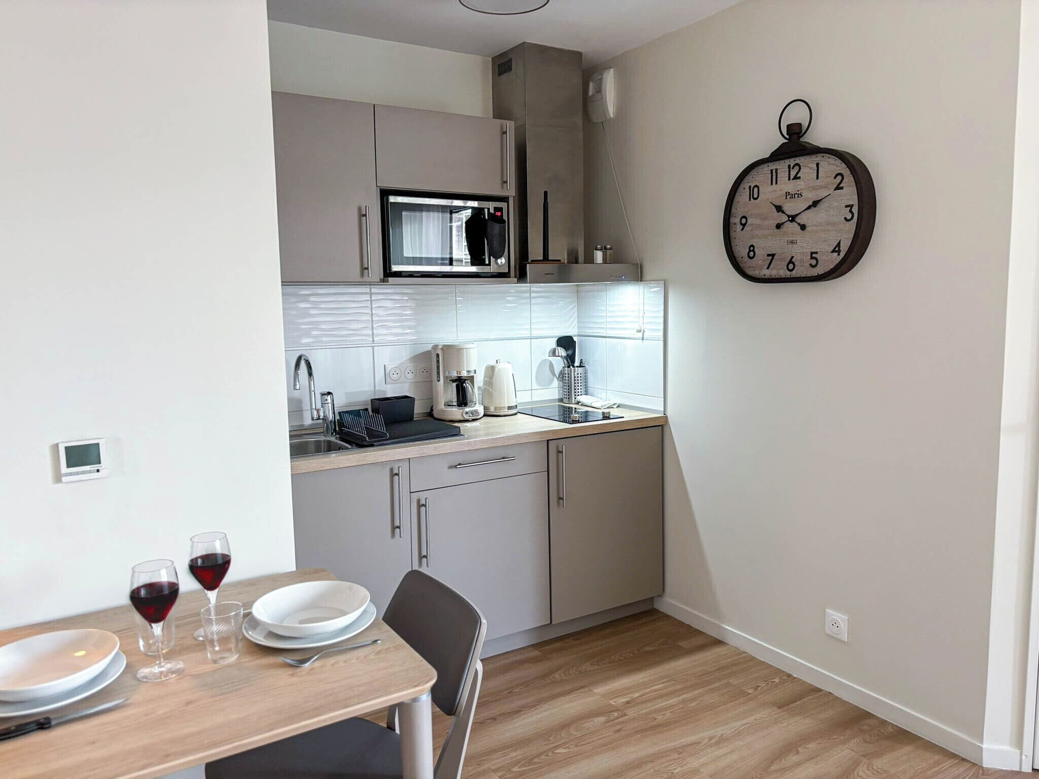 Een kleine keuken met een magnetron, koffiezetapparaat en een klok aan de muur.