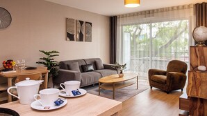 Ein modernes Wohnzimmer mit einer Couch, einem Sessel, einem Couchtisch und einem Essbereich mit Tisch und Stühlen. Es gibt ein großes Fenster mit Vorhängen, eine Uhr an der Wand und einen Globus auf einem Holzständer.