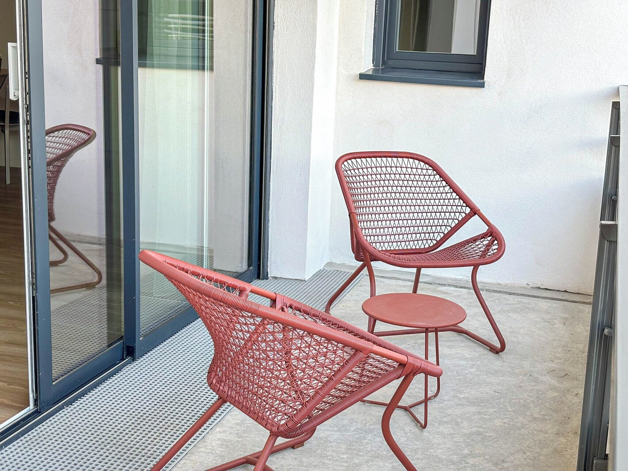 A glass door leading to a balcony with two red wicker chairs and a small table.