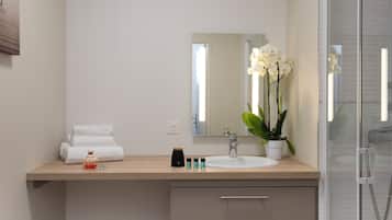 A modern bathroom with a wooden vanity, a large mirror, a white sink, and a potted orchid.
