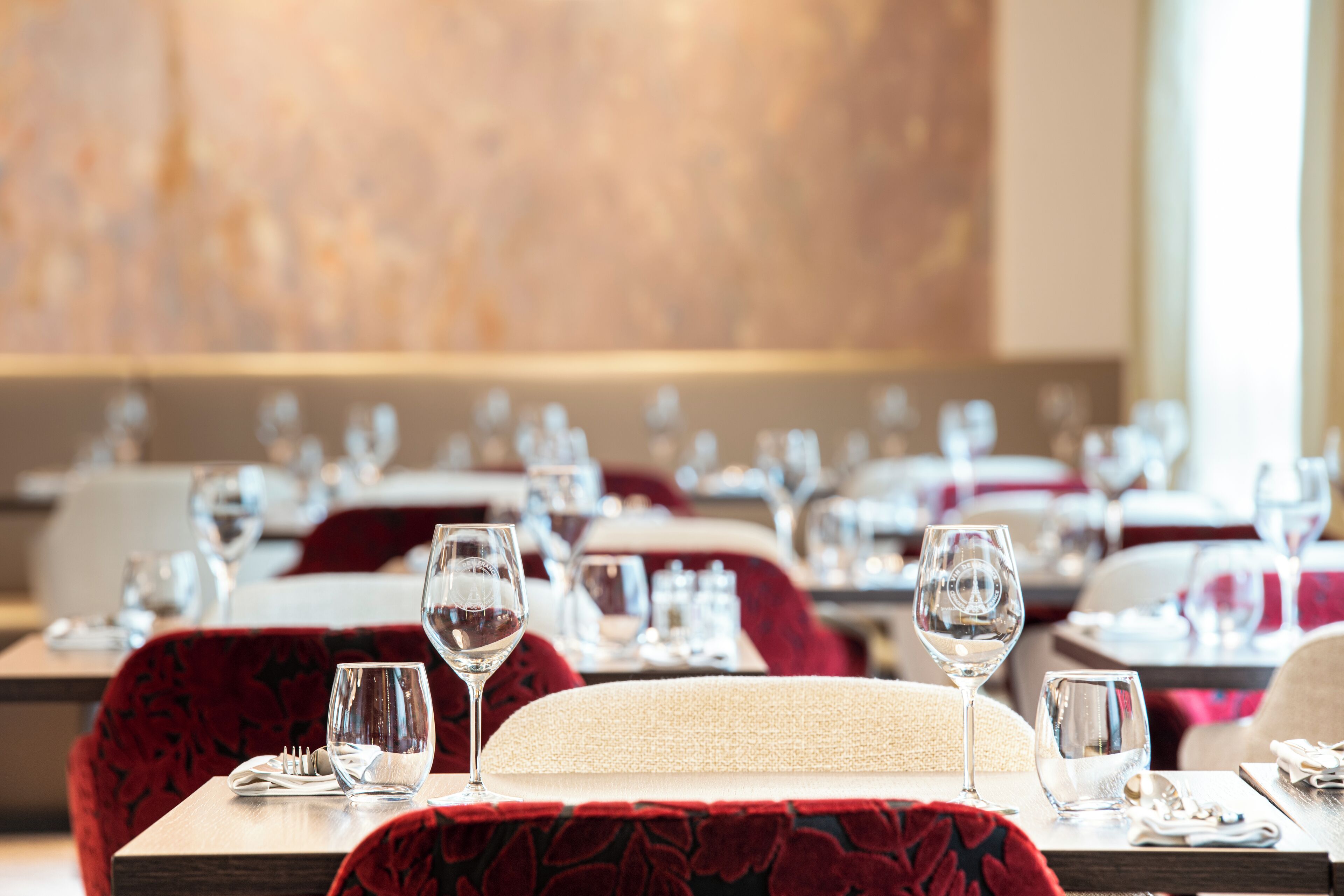 Un restaurante con mesas dispuestas para comer, con sillas tapizadas en rojo y mantel de tonos neutros.