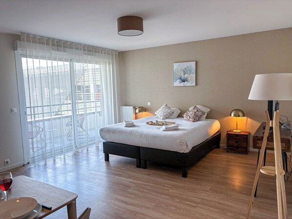 Un dormitorio moderno con una cama grande, lámparas de noche, un cuadro en la pared y un balcón con sillas.