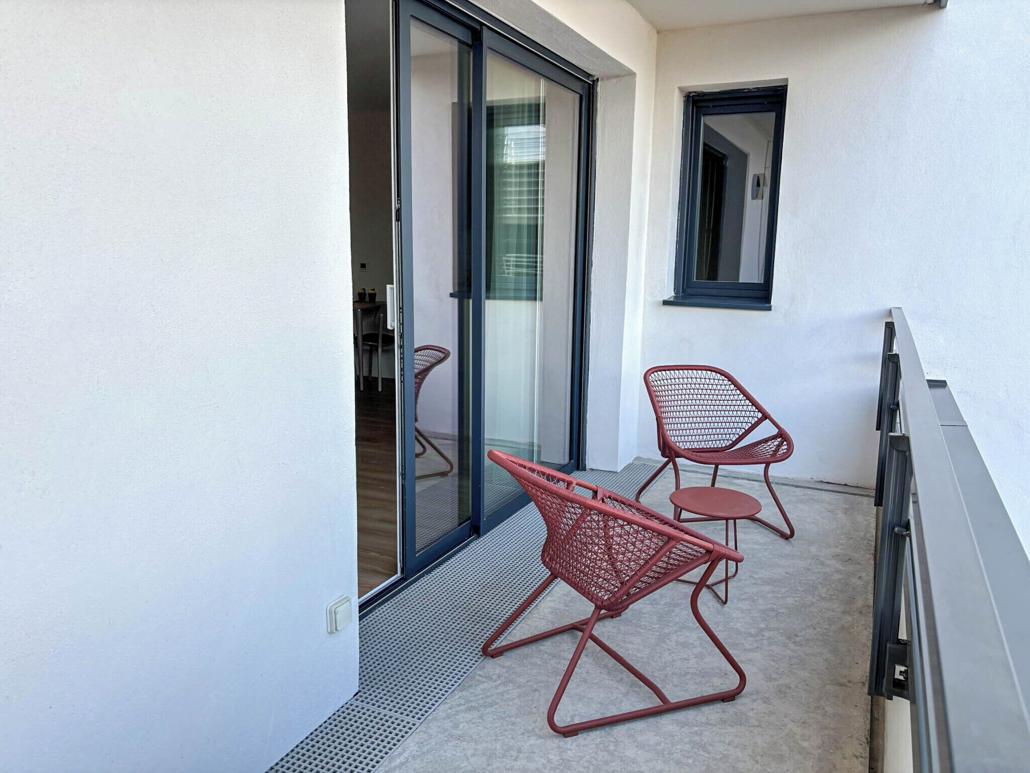 Een balkon met twee rode stoelen van netstof, een schuifdeur en een klein raam.