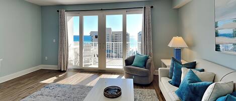A living room with a white sofa, blue cushions, a coffee table, and a view of the ocean through large sliding doors.