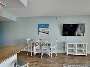 A living room with a dining table, chairs, a TV, and a painting on the wall. - Laketown Wharf #913 | Beautiful Condo, Stunning View + Resort Amenities (Panama City Beach)