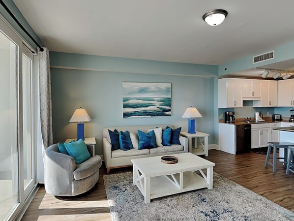A living room with a sofa, two side tables, a coffee table, and a painting of the ocean. - Laketown Wharf #913 | Beautiful Condo, Stunning View + Resort Amenities (Panama City Beach)