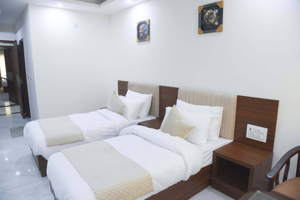 A hotel room with two beds, a wooden headboard, a nightstand, and a wall-mounted power outlet.