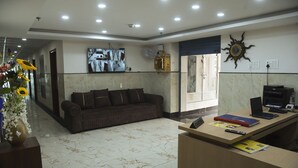 Una hall d'albergo con reception, divano, televisore a parete e orologio solare decorativo.