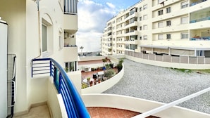 A multi-story residential building with balconies, a courtyard with seating and plants, and a view of the sea.