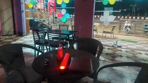 Un espace extérieur aménagé avec des chaises et des tables en osier, une enseigne Coca-Cola et des ballons de couleurs vives.