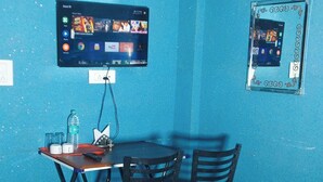 Une pièce avec un mur bleu, un lit recouvert d’une courtepointe à motifs rouges et blancs, un bureau avec deux chaises, un téléviseur fixé au mur et un tableau encadré accroché au mur.