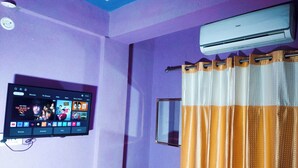Une pièce équipée d’un téléviseur fixé au mur qui affiche l’interface d’un service de diffusion en continu, d’un appareil de climatisation et d’un rideau.