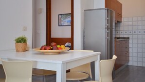 A compact kitchen with a refrigerator, a dining table with chairs, and a fruit bowl. - Stylish and bright apartment (Bibione)