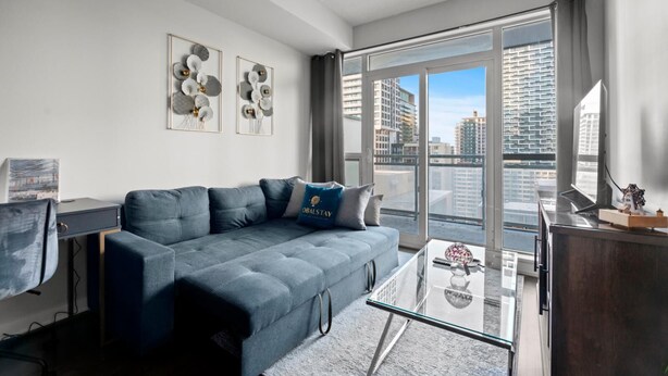 A modern living room with a grey sofa, a glass coffee table, and a city view through large windows. - GLOBALSTAY Modern 1BD+Den Condo w/ Balcony Lillian St (Toronto/Canada)