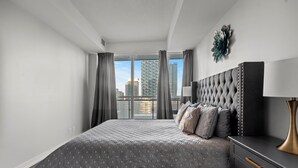 A modern bedroom with a large bed, a nightstand, a lamp, and a view of tall buildings through large windows. - GLOBALSTAY Modern 1BD+Den Condo w/ Balcony Lillian St (Toronto/Canada)