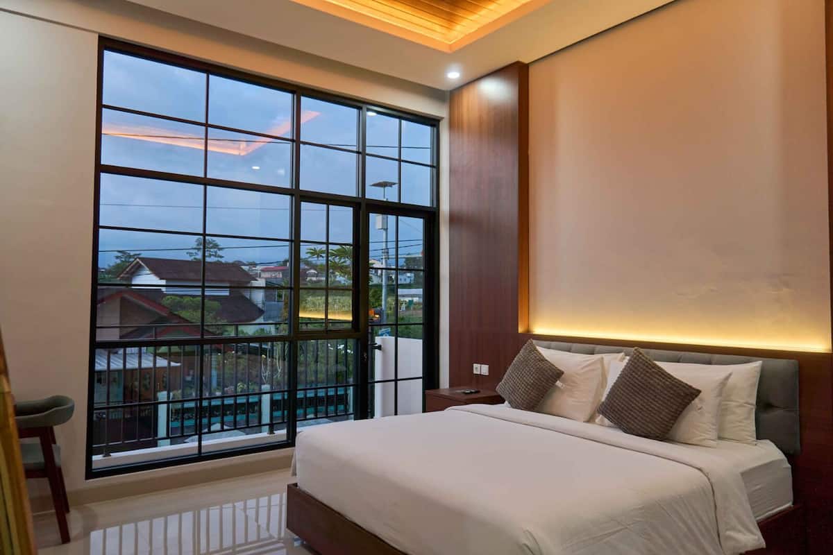 Un dormitorio con un ventanal grande, una cama con almohadas y una mesita de noche.