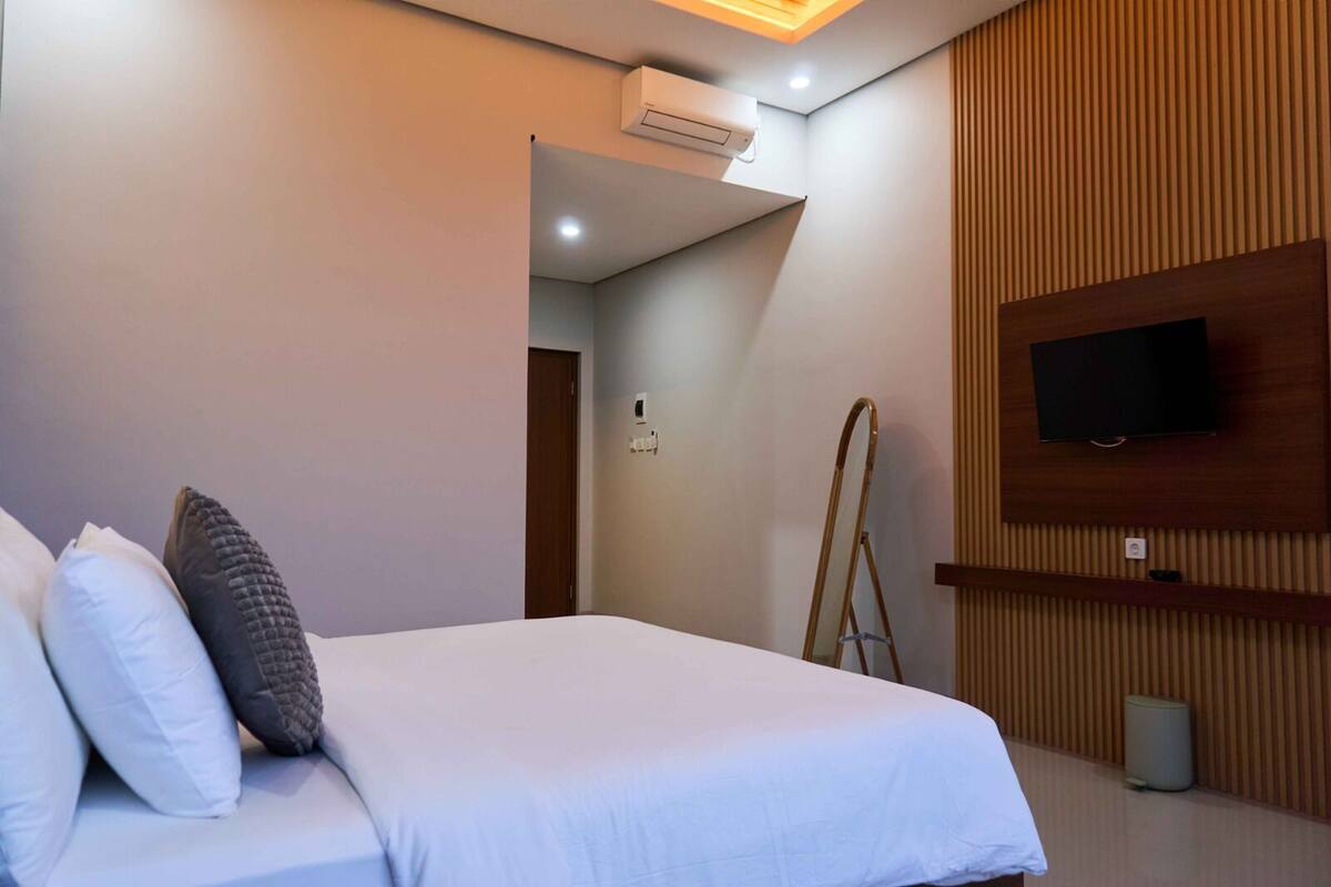 Una habitación de hotel con una cama, un televisor montado en la pared y paneles de madera decorativos.