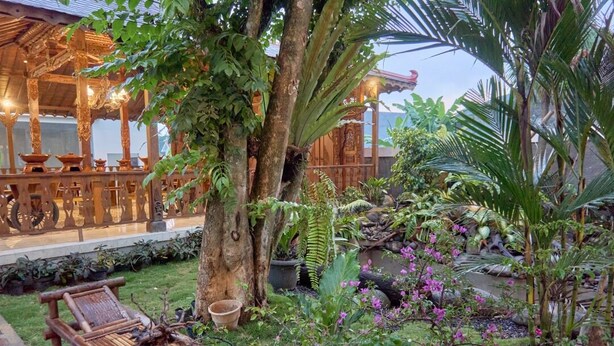 A wooden gazebo with intricate carvings, surrounded by lush greenery and flowering plants. - Sakanti Inn Wonosobo (Wonosobo)