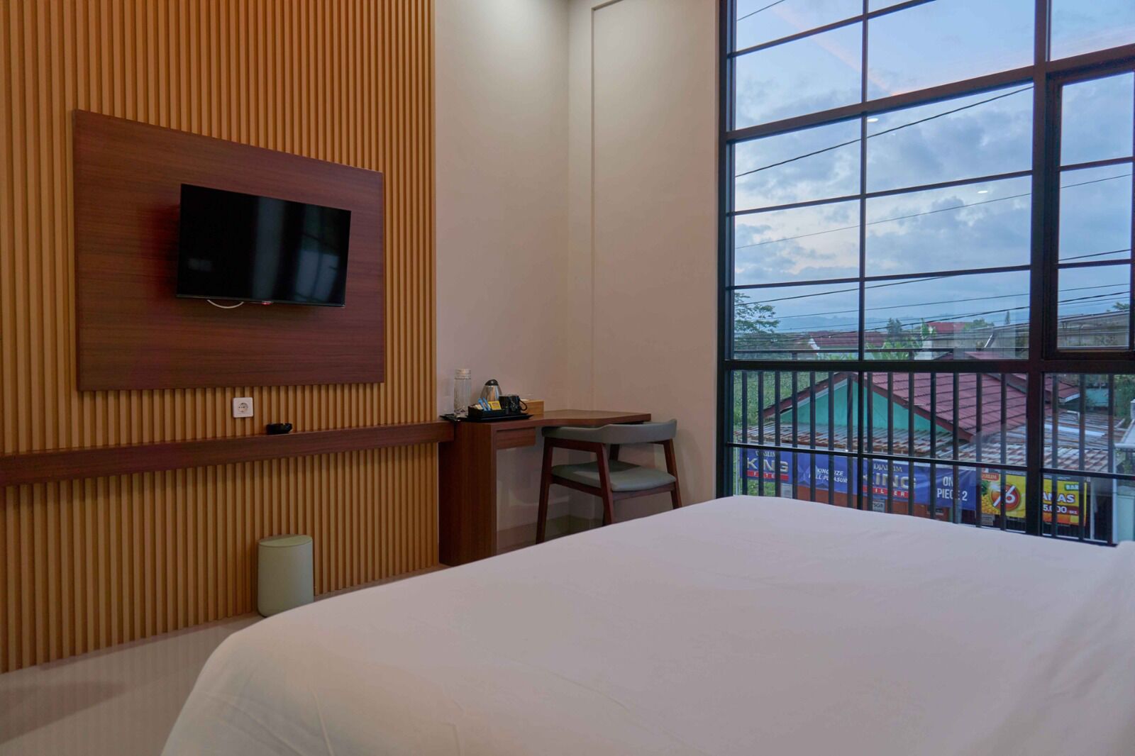 Ein Hotelzimmer mit Bett, Schreibtisch, Stuhl, einem an einer Holzverkleidung befestigten Fernseher und einem großen Fenster mit Blick nach außen.