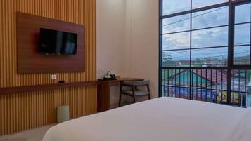 Ein Hotelzimmer mit Bett, Schreibtisch, Stuhl, einem an einer Holzverkleidung befestigten Fernseher und einem großen Fenster mit Blick nach außen.